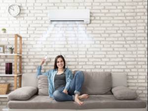 A woman sitting on the couch in front of an air conditioner.